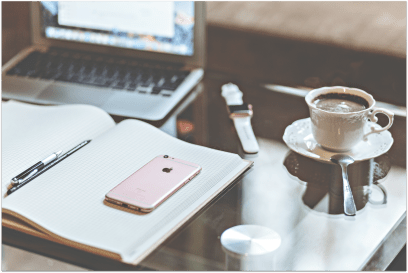 Desktop with laptop computer, open journal, pen, iPhone, cup of coffee