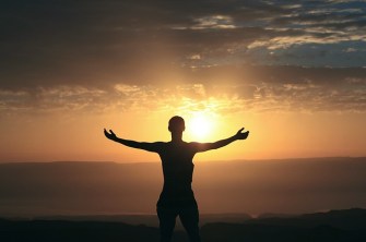 Person feeling gratitude looking at the sunrise with extended arms