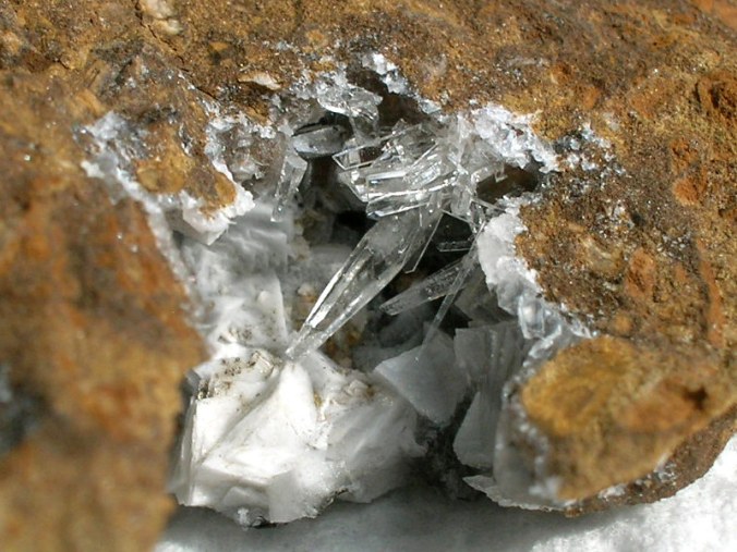 Closeup photo ofVug with aragonite & calcite crystals in arenaceous, ferruginous, fossiliferous limestone